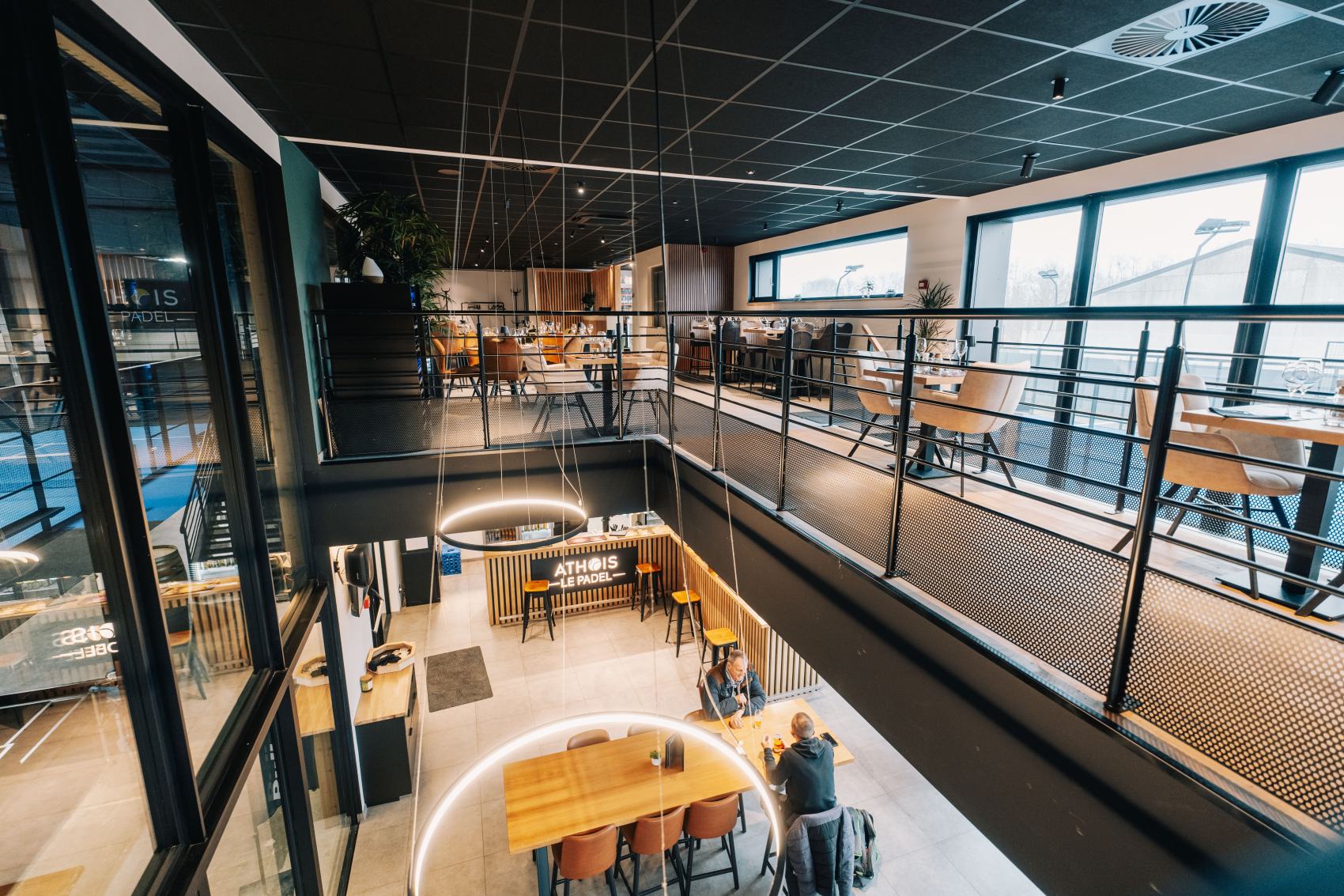 Le Bel Effet vu depuis la mezzanine : le bar, la double hauteur et les terrains derrière les baies vitrées