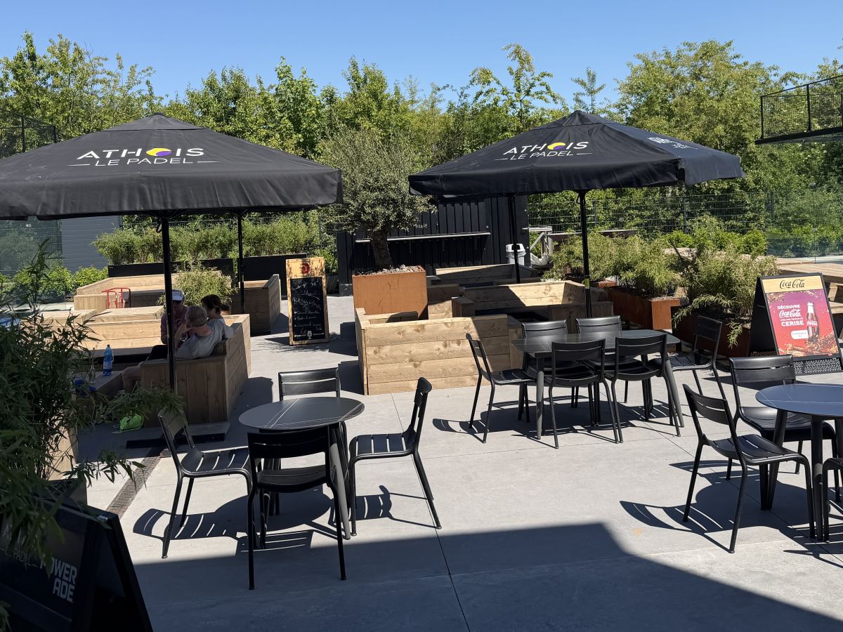 La terrasse du club, ses parasols et ses tables face aux terrains extérieurs